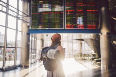 Tema seyahat ve tranosport. Güzel genç kafkas kadın elbise ve tren istasyonuna veya kırmızı telefon tutarak bir zamanlama seyir terminal içinde duran sırt çantası iletişim teknolojisini kullanır