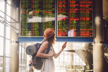 Tema seyahat ve tranosport. Güzel genç kafkas kadın elbise ve tren istasyonuna veya kırmızı telefon tutarak bir zamanlama seyir terminal içinde duran sırt çantası iletişim teknolojisini kullanır