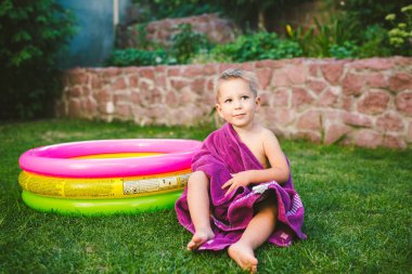 Yaz tatil tema. Kuru bir havlu kırmızı yüzme şort olmak yok, yuvarlak bir şişme renkli havuz yakınındaki çimenlerin üzerinde bir evin arka bahçesinde oynarken küçük 3 yaşındaki beyaz çocuk sarılmış.