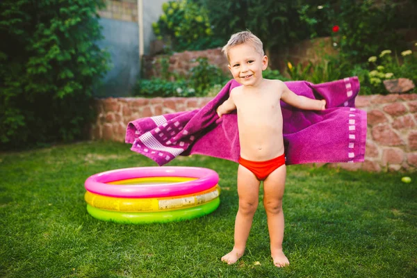 夏の休暇のテーマ ラウンド膨脹可能な色のプールのそばの芝生の家の裏庭で遊んで小さな 歳の白人少年を包んだ 赤い水泳パンツに乾いたタオルを一掃 — ストック写真