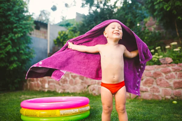 夏の休暇のテーマ ラウンド膨脹可能な色のプールのそばの芝生の家の裏庭で遊んで小さな 歳の白人少年を包んだ 赤い水泳パンツに乾いたタオルを一掃 — ストック写真