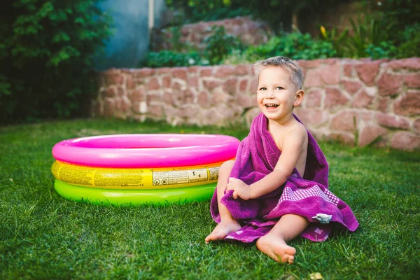 Yaz tatil tema. Kuru bir havlu kırmızı yüzme şort olmak yok, yuvarlak bir şişme renkli havuz yakınındaki çimenlerin üzerinde bir evin arka bahçesinde oynarken küçük 3 yaşındaki beyaz çocuk sarılmış.