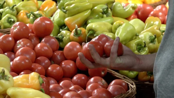 Tema hälsa och naturlig mat. Närbild av en kaukasiska man holding, plocka tomater i en vtrine i en stormarknad box hand. Vegetarisk kille köper röda grönsaker — Stockfoto