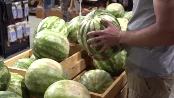Thema gezondheid en natuurlijke voeding. Close-up van een Kaukasische mans hand houdt, selecteert een watermeloen in een vetrine in een doos van de supermarkt. Vegetarische man koopt een groene sappige bessen — Stockvideo