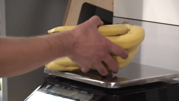 Tema salute e cibo naturale. Primo piano della mano di un caucasico che pesa un mucchio di banane. Un vegetariano compra un frutto giallo — Video Stock