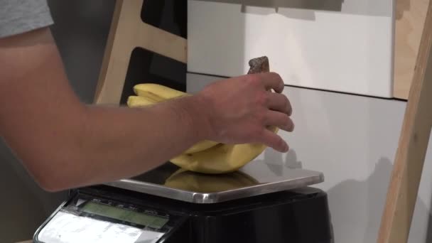 Tema salute e cibo naturale. Primo piano della mano di un caucasico che pesa un mucchio di banane. Un vegetariano compra un frutto giallo — Video Stock