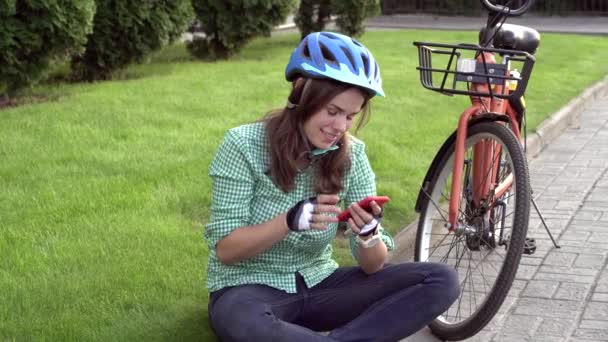 人間と都市の圧延自転車 環境に優しい輸送 草の上に座っている美しい若い白人女性労働者は コーリンとオレンジの自転車の近くに赤い携帯電話を使用しています — ストック動画