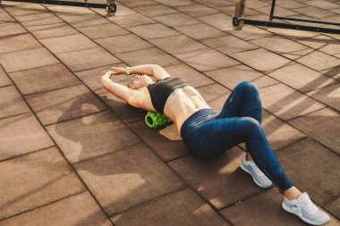theme sport and rehabilitation sports medicine. Beautiful strong slender Caucasian woman athlete uses foam roller green field street workout to workout to remove pain, stretch and massage muscles. clipart