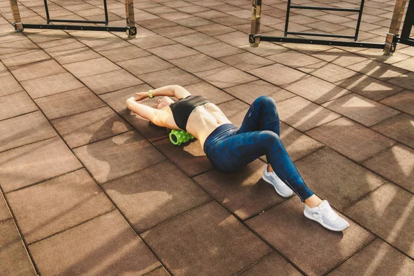 theme sport and rehabilitation sports medicine. Beautiful strong slender Caucasian woman athlete uses foam roller green field street workout to workout to remove pain, stretch and massage muscles.