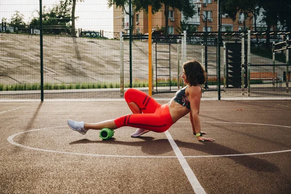 theme sport and rehabilitation sports medicine. Beautiful strong slender Caucasian woman athlete uses foam roller green field street workout to workout to remove pain, stretch and massage muscles.