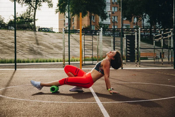 theme sport and rehabilitation sports medicine. Beautiful strong slender Caucasian woman athlete uses foam roller green field street workout to workout to remove pain, stretch and massage muscles.