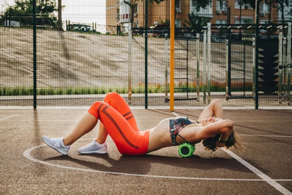 theme sport and rehabilitation sports medicine. Beautiful strong slender Caucasian woman athlete uses foam roller green field street workout to workout to remove pain, stretch and massage muscles.