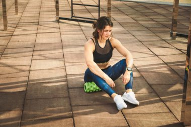 Tema spor ve rehabilitasyon spor hekimliği. Güzel güçlü ince beyaz kadın atlet ağrı kaldırmak, esneme ve kaslar masaj sonraki köpük rulo yeşil alan sokak iş oturur.