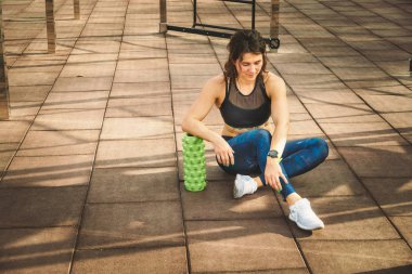 Tema spor ve rehabilitasyon spor hekimliği. Güzel güçlü ince beyaz kadın atlet ağrı kaldırmak, esneme ve kaslar masaj sonraki köpük rulo yeşil alan sokak iş oturur.