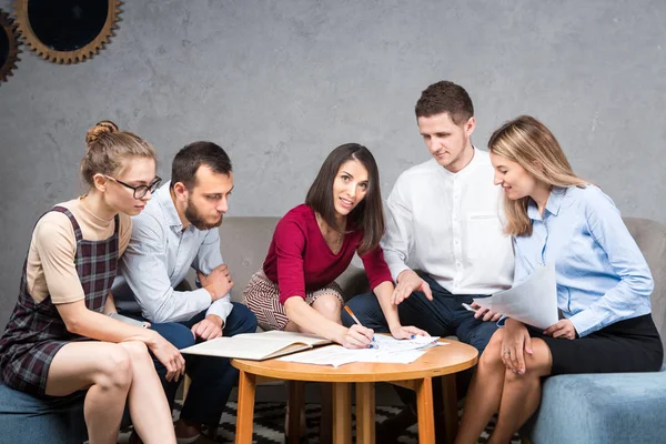 Subject business situation, teamwork. Group of young Caucasian five people sitting in office at a round table meeting, using paper, graphics.