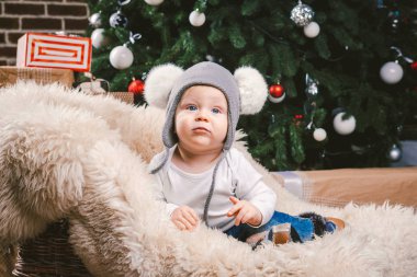 Konu çocuk Noel yeni yıl. Beyaz küçük komik bebek çocuk 1 yaşında oturma atlı kızak ayı cilt balabons topları ile Noel ağacı baş sıcak şapka, topları ve çevresinde kot kutu hediyeler akşam.