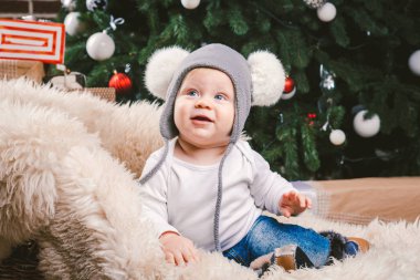 Konu çocuk Noel yeni yıl. Beyaz küçük komik bebek çocuk 1 yaşında oturma atlı kızak ayı cilt balabons topları ile Noel ağacı baş sıcak şapka, topları ve çevresinde kot kutu hediyeler akşam.