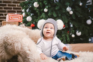Konu çocuk Noel yeni yıl. Beyaz küçük komik bebek çocuk 1 yaşında oturma atlı kızak ayı cilt balabons topları ile Noel ağacı baş sıcak şapka, topları ve çevresinde kot kutu hediyeler akşam.