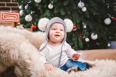 Konu çocuk Noel yeni yıl. Beyaz küçük komik bebek çocuk 1 yaşında oturma atlı kızak ayı cilt balabons topları ile Noel ağacı baş sıcak şapka, topları ve çevresinde kot kutu hediyeler akşam.