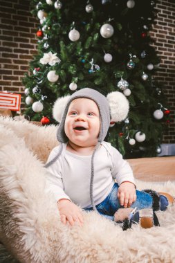 Konu çocuk Noel yeni yıl. Beyaz küçük komik bebek çocuk 1 yaşında oturma atlı kızak ayı cilt balabons topları ile Noel ağacı baş sıcak şapka, topları ve çevresinde kot kutu hediyeler akşam.