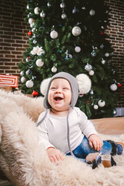 Konu çocuk Noel yeni yıl. Beyaz küçük komik bebek çocuk 1 yaşında oturma atlı kızak ayı cilt balabons topları ile Noel ağacı baş sıcak şapka, topları ve çevresinde kot kutu hediyeler akşam.