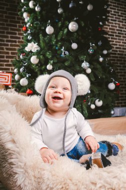Konu çocuk Noel yeni yıl. Beyaz küçük komik bebek çocuk 1 yaşında oturma atlı kızak ayı cilt balabons topları ile Noel ağacı baş sıcak şapka, topları ve çevresinde kot kutu hediyeler akşam.