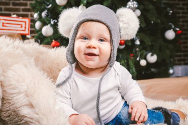 Konu çocuk Noel yeni yıl. Beyaz küçük komik bebek çocuk 1 yaşında oturma atlı kızak ayı cilt balabons topları ile Noel ağacı baş sıcak şapka, topları ve çevresinde kot kutu hediyeler akşam.