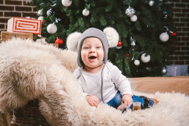 Konu çocuk Noel yeni yıl. Beyaz küçük komik bebek çocuk 1 yaşında oturma atlı kızak ayı cilt balabons topları ile Noel ağacı baş sıcak şapka, topları ve çevresinde kot kutu hediyeler akşam.