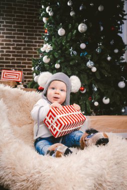 Konu çocuk Noel yeni yıl. Beyaz küçük komik bebek çocuk 1 yaşında oturma atlı kızak ayı cilt balabons topları ile Noel ağacı baş sıcak şapka, topları ve çevresinde kot kutu hediyeler akşam.