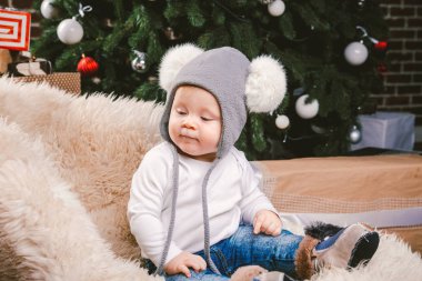 Konu çocuk Noel yeni yıl. Beyaz küçük komik bebek çocuk 1 yaşında oturma atlı kızak ayı cilt balabons topları ile Noel ağacı baş sıcak şapka, topları ve çevresinde kot kutu hediyeler akşam.