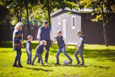 Tema aile açık hava etkinlikleri. altı anne baba büyük dostu beyaz ailesi ve dört çocuk futbol topu ile çim üzerinde çalışan, güneşli bir günde evin yanında çim çim yeşil.