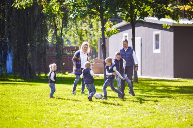 Tema aile açık hava etkinlikleri. altı anne baba büyük dostu beyaz ailesi ve dört çocuk futbol topu ile çim üzerinde çalışan, güneşli bir günde evin yanında çim çim yeşil.