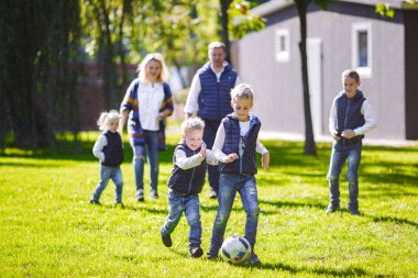 Tema aile açık hava etkinlikleri. altı anne baba büyük dostu beyaz ailesi ve dört çocuk futbol topu ile çim üzerinde çalışan, güneşli bir günde evin yanında çim çim yeşil.