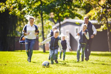 Tema aile açık hava etkinlikleri. altı anne baba büyük dostu beyaz ailesi ve dört çocuk futbol topu ile çim üzerinde çalışan, güneşli bir günde evin yanında çim çim yeşil.