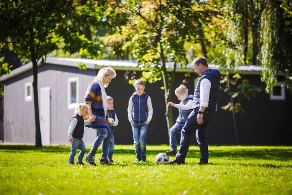 The theme family outdoor activities. big friendly Caucasian family of six mom dad and four children playing football, running with the ball on lawn, green grass lawn near the house on a sunny day.