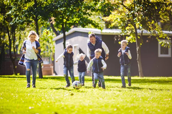 The theme family outdoor activities. big friendly Caucasian family of six mom dad and four children playing football, running with the ball on lawn, green grass lawn near the house on a sunny day.