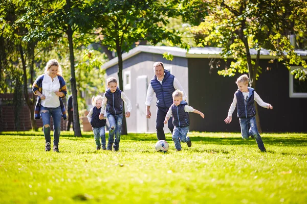 The theme family outdoor activities. big friendly Caucasian family of six mom dad and four children playing football, running with the ball on lawn, green grass lawn near the house on a sunny day.