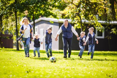Tema aile açık hava etkinlikleri. altı anne baba büyük dostu beyaz ailesi ve dört çocuk futbol topu ile çim üzerinde çalışan, güneşli bir günde evin yanında çim çim yeşil.