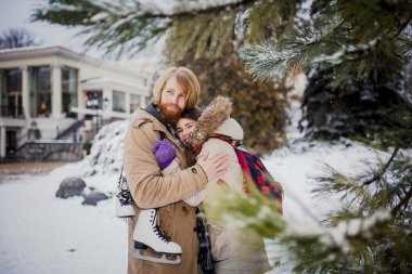 Sarı uzun saçları ve sakalı ile genç sevgi dolu çift beyaz adam, kadın dişlek gülümseme ile iyi eğlenceler şımartın, etrafında Noel ağacı Kış Parkı, iğne yapraklı ağaç buz pateni kış aylarında sonra aptal,.