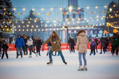 Uzun saçlı sarışın saçlı beyaz adam genç çift tr ve eğlenceli, aktif tarihi buz pateni Buz arenada akşam şehir meydanında Noel arifesinde kışın sakal ve güzel bir kadın var