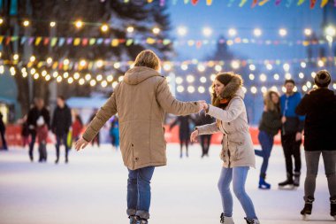 Uzun saçlı sarışın saçlı beyaz adam genç çift tr ve eğlenceli, aktif tarihi buz pateni Buz arenada akşam şehir meydanında Noel arifesinde kışın sakal ve güzel bir kadın var