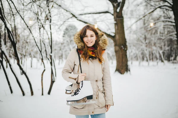 主题是冬天的周末假期 一个美丽的年轻白种女人站在雪盖公园夹克与头巾和毛皮的牛仔裤 并持有双肩白色冰鞋长鞋带 — 图库照片