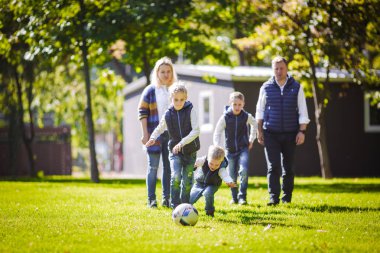 Tema aile açık hava etkinlikleri. altı anne baba büyük dostu beyaz ailesi ve dört çocuk futbol topu ile çim üzerinde çalışan, güneşli bir günde evin yanında çim çim yeşil.