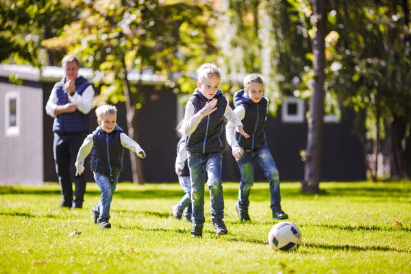 The theme family outdoor activities. big friendly Caucasian family of six mom dad and four children playing football, running with the ball on lawn, green grass lawn near the house on a sunny day.