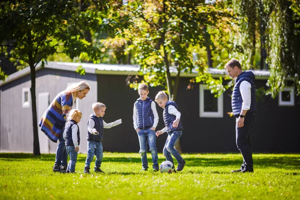 The theme family outdoor activities. big friendly Caucasian family of six mom dad and four children playing football, running with the ball on lawn, green grass lawn near the house on a sunny day.