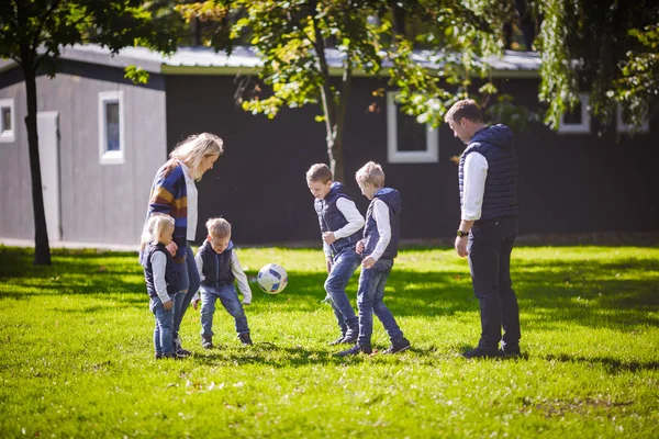 The theme family outdoor activities. big friendly Caucasian family of six mom dad and four children playing football, running with the ball on lawn, green grass lawn near the house on a sunny day.