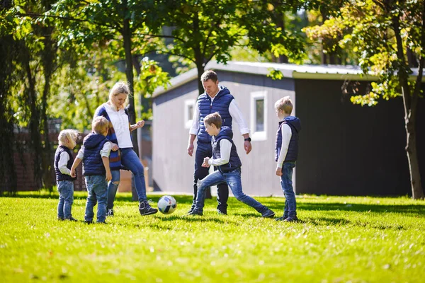 The theme family outdoor activities. big friendly Caucasian family of six mom dad and four children playing football, running with the ball on lawn, green grass lawn near the house on a sunny day.