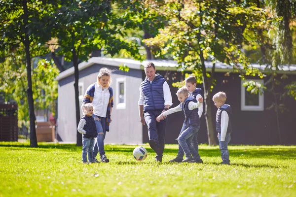 The theme family outdoor activities. big friendly Caucasian family of six mom dad and four children playing football, running with the ball on lawn, green grass lawn near the house on a sunny day.