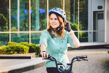 Motosiklet üzerinde çalışmak için tema. Genç beyaz bir kadın ofise çevre dostu bir taşıma bisikletiyle geldi. Bisikletli park yerindeki kask, eldiven, gömlek ve kot pantolon giyen bir kız..