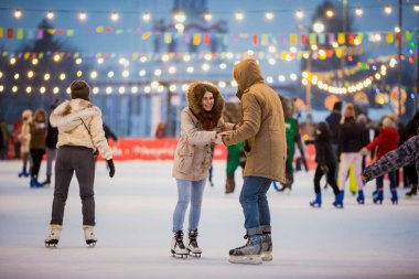 Uzun saçlı sarışın saçlı beyaz adam genç çift tr ve eğlenceli, aktif tarihi buz pateni Buz arenada akşam şehir meydanında Noel arifesinde kışın sakal ve güzel bir kadın var